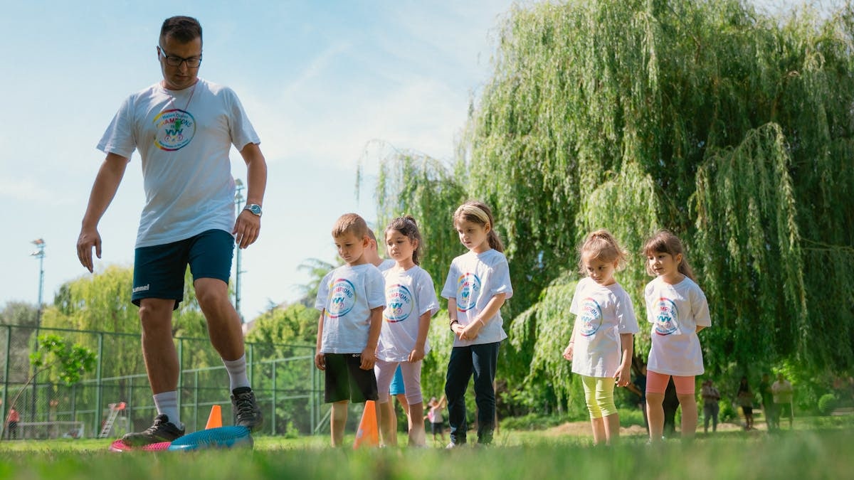 Children in a park learning sports with a coach on a sunny day.